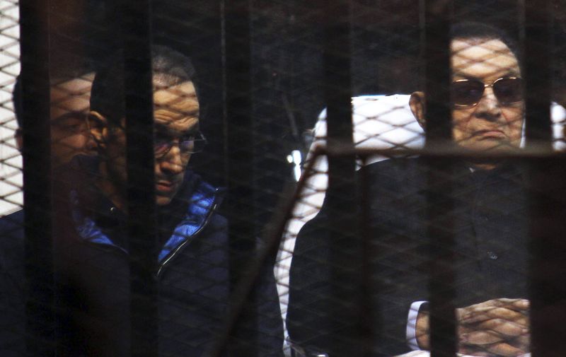 Former Egyptian President Hosni Mubarak listens next to his son Gamal inside a dock during his trial at the police academy on the outskirts of Cairo